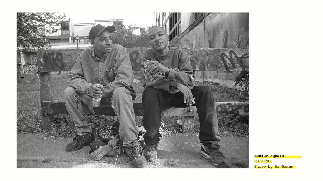 Black and white photo of two young men sitting on a curb outside Hulme Crescents, credited to Al Baker
