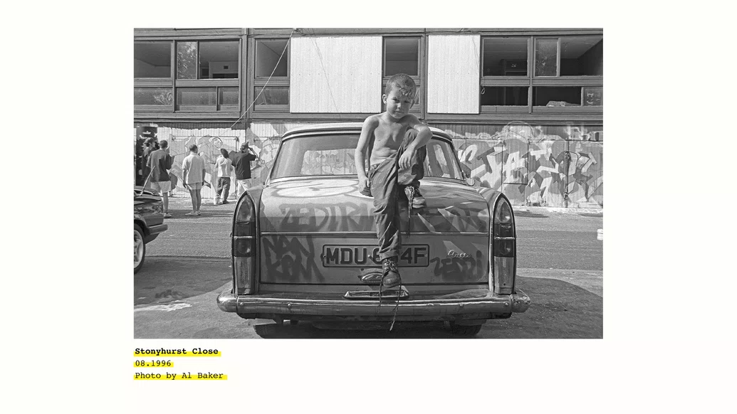 black and white photo of a young boy sitting on the hood of a car in hulme crescents credited to Al Baker