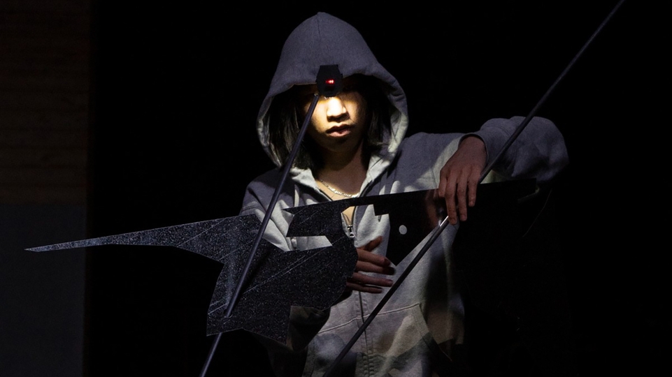 Lavurn in a dark room with a hood up holding a shard of metal