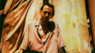 Photo of Luca Venezia sitting against a pillar wearing a beige shirt and sunglasses