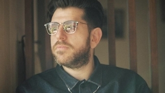Photo of Moscoman wearing a denim shirt and glasses in a wooden-panelled room