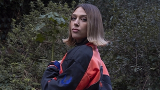 re:ni poses in a forest wearing a black blue and red racing jacket