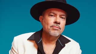 Photo of Louie Vega wearing a black shirt and hat with a white blazer