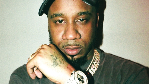 Photo of Benny the Butcher wearing a black t-shirt and hat with gold chains and a watch
