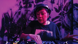 Photo of Hiroko Yamamura DJing on CDjs under a pinkish purple light