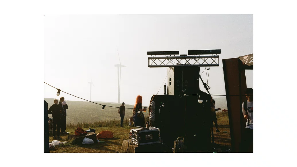 Photo of a ravers at a free party on a hill with wind turbines in the background