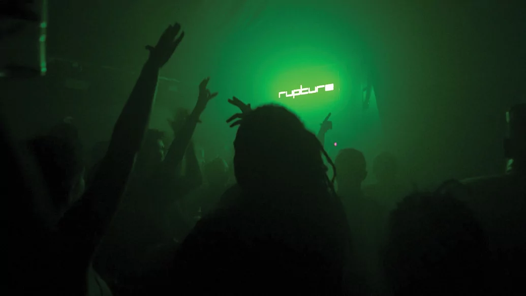 Shot of a crowd at a Rupture party, beneath a green glowing Rupture logo