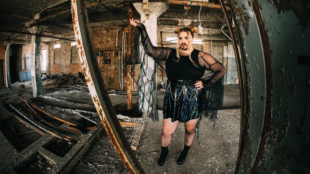 Wreckno standing in a derelict building in a black skirt and top with flowing extensions and hair in buns