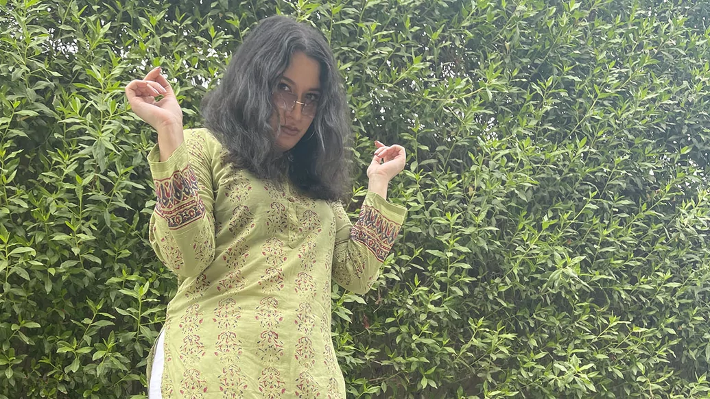 Manara posing in a green kameez in front of a hedge
