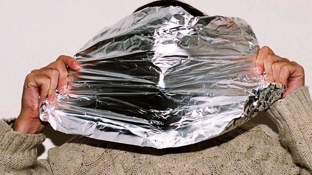 Photo of John Talabot wearing an off-white wooly sweater holding a sheet of tinfoil over his face