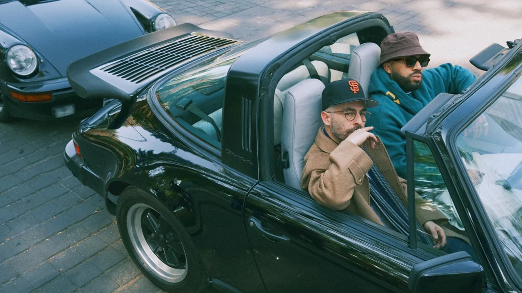 The Alchemist and Larry June are sat next to eachother in a convertible black vintage car