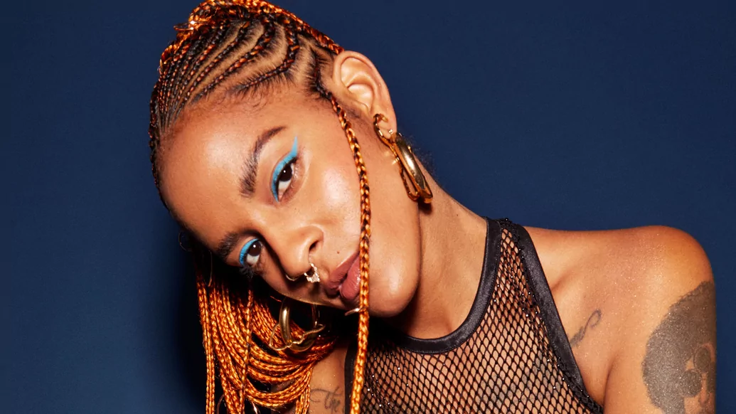 Photo of Coco smiling with her hair in braids in front of a blue background