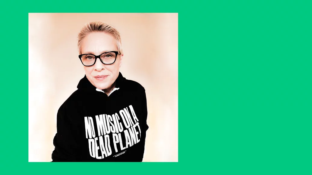 Photo of Liz Somes wearing a ‘No Music On A Dead Planet’ hoodie on a green background with her name printed