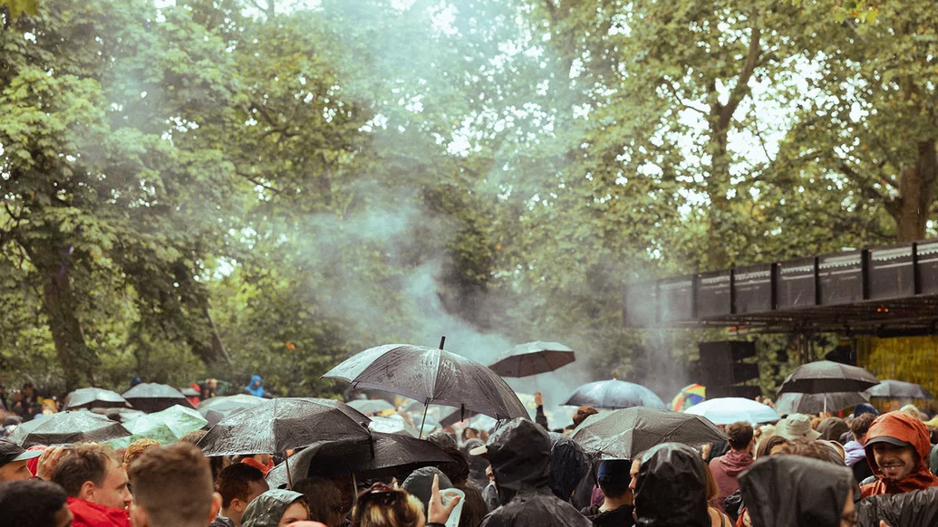 Crowd shot full of umbrellas of the Visionaire stage surrounded by trees at Rally festival with a plume of smoke coming from the stage