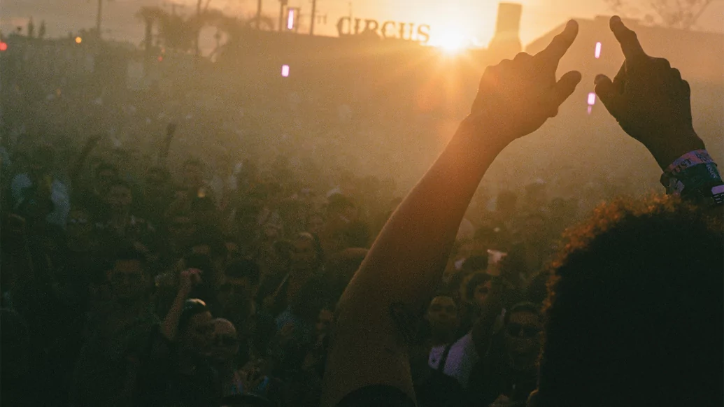 Photo of a hazy crowd at a festival with Damian Lazarus holding up his hands in the foreground