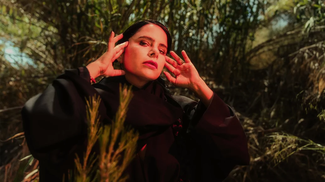 Photo of Sofia Kourtesis wearing a black cape in front of some trees