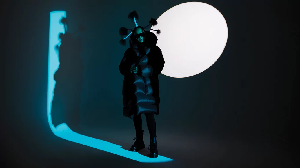 Photo of HoneyLuv under a blue spotlight wearing a black puffer and vertical braids in her hair 