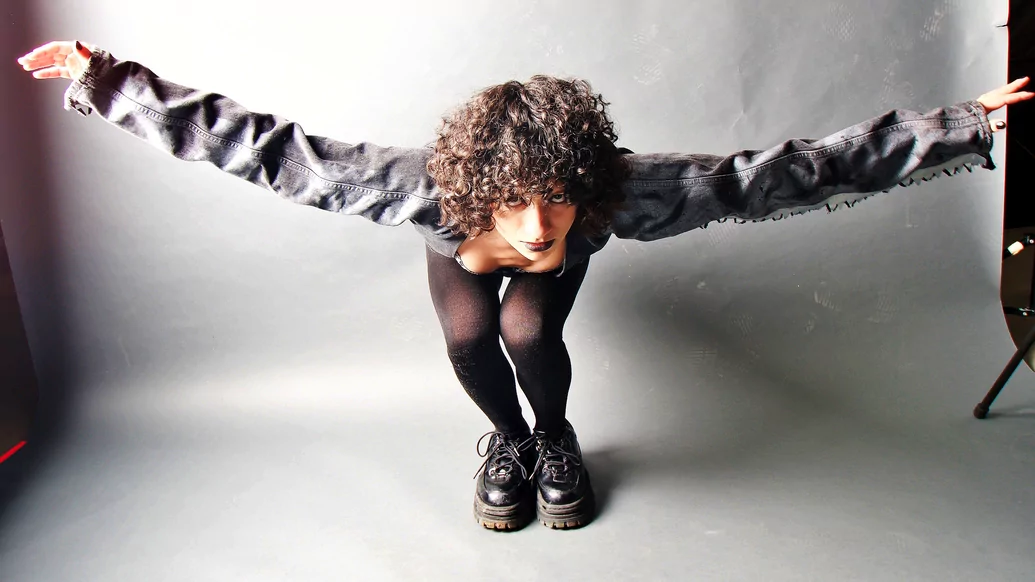 Photo of Julie Pavon bowing in a photo studio wearing a grey jacket and big black boots