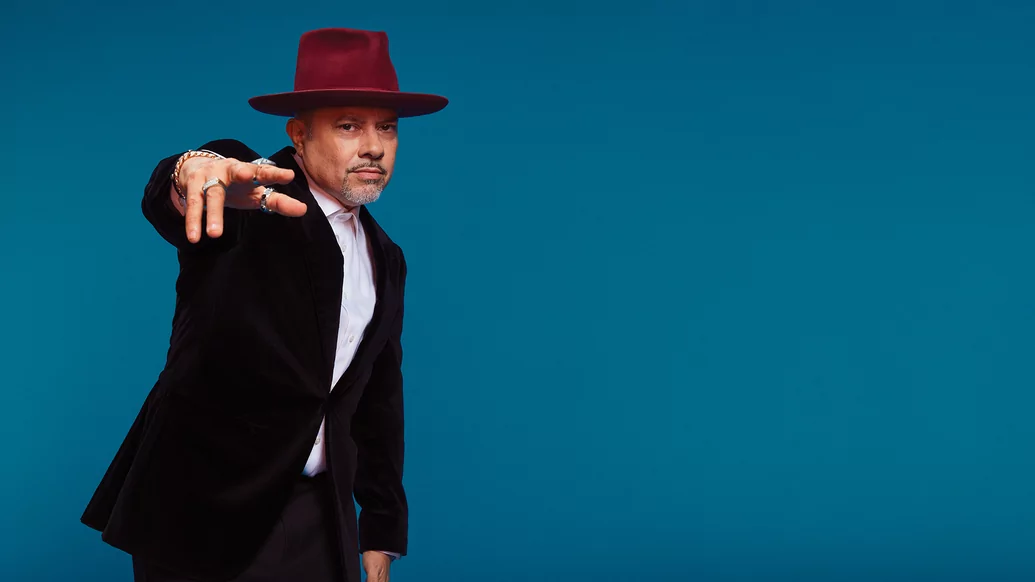 Photo of Louie Vega wearing a black shirt, red hat and white blazer
