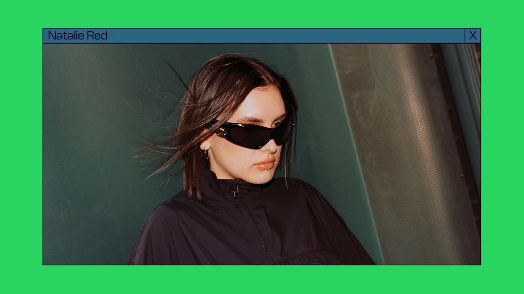 Photo of Natalie Red wearing large black sunglasses on a bright green background