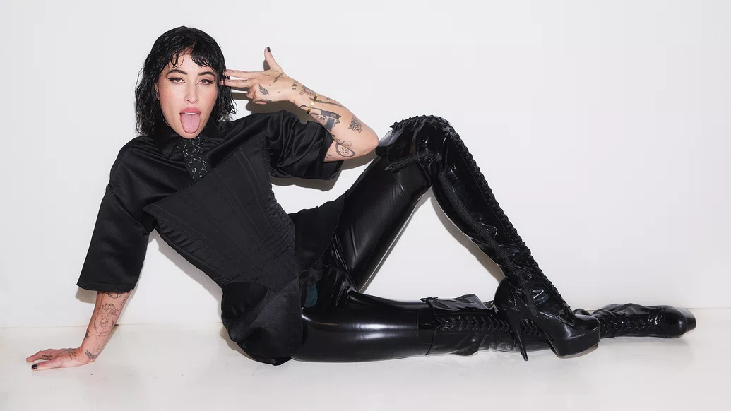 Photo of Indira Paganotto wearing a black catsuit whilst posing on her side