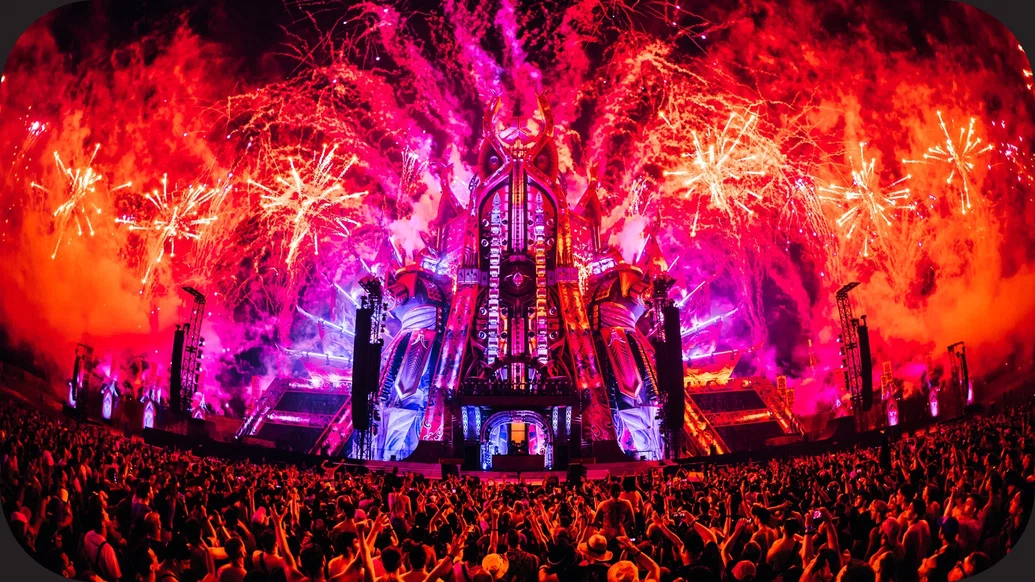 Photo of the Defqon.1 stage with pink, orange and purple lights and a big crowd
