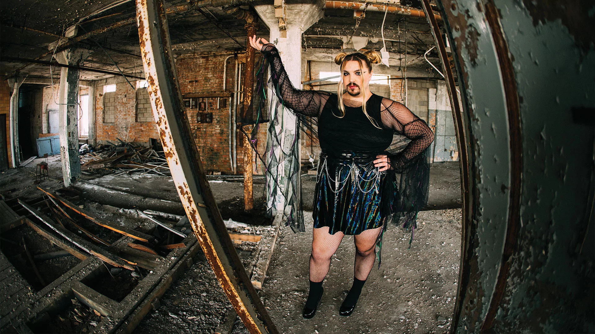 Wreckno standing in a derelict building in a black skirt and top with flowing extensions and hair in buns