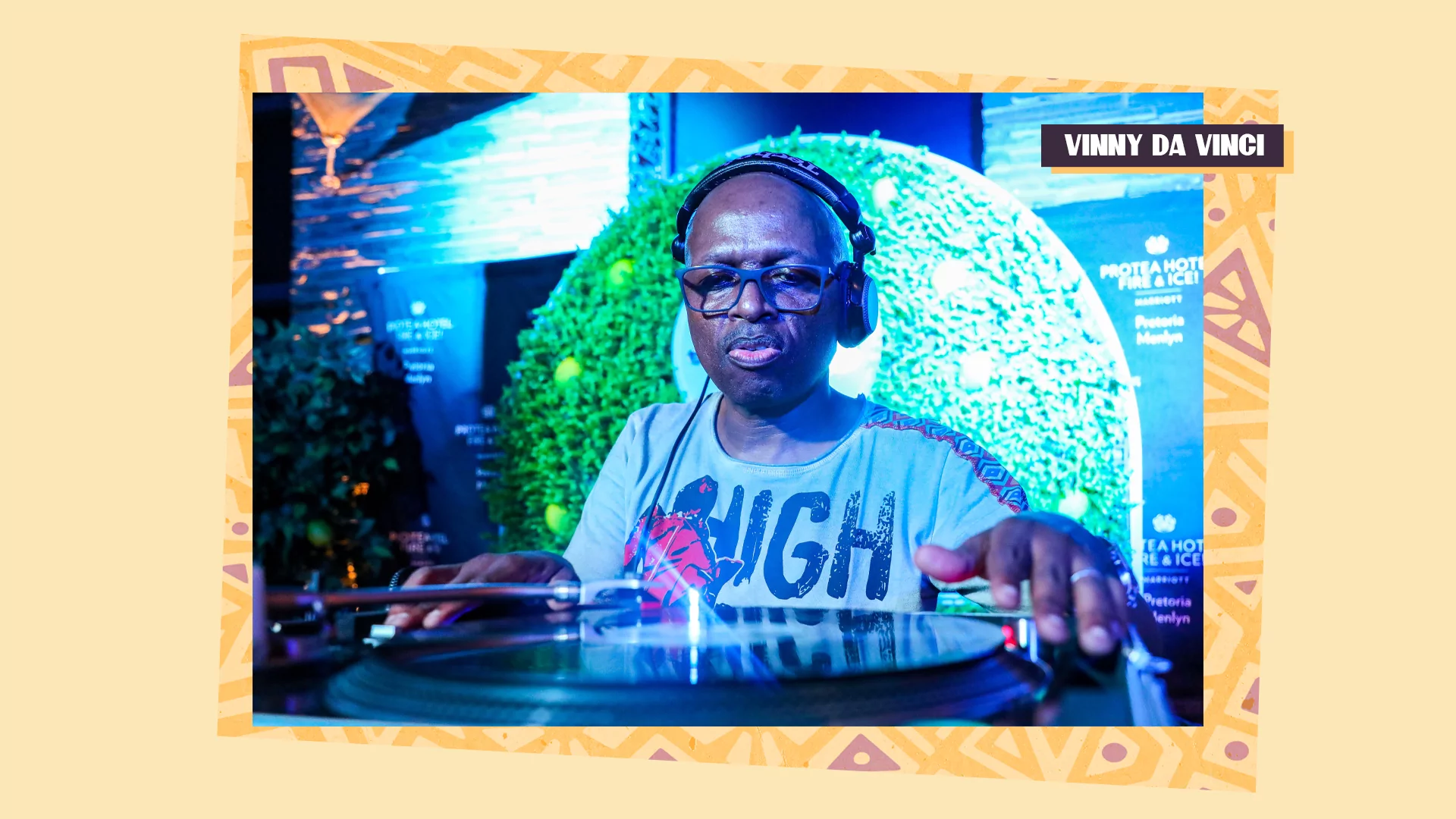 DJ Vinny Da Vinci playing vinyl in a club in front of a green wreath and blue light