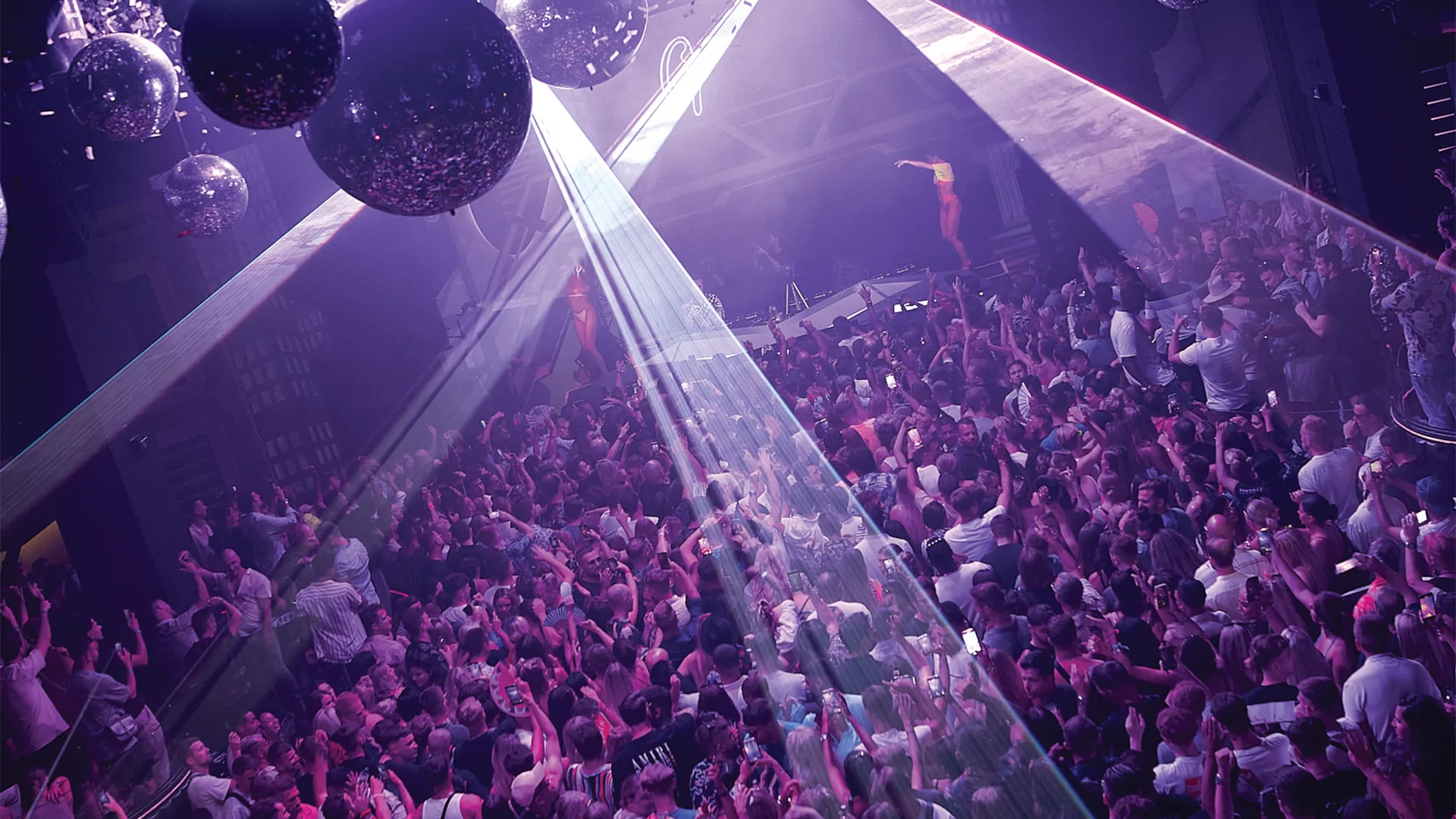Ariel shot of a crowded nightclub under a purple light, with Purple Disco Machine behind the decks