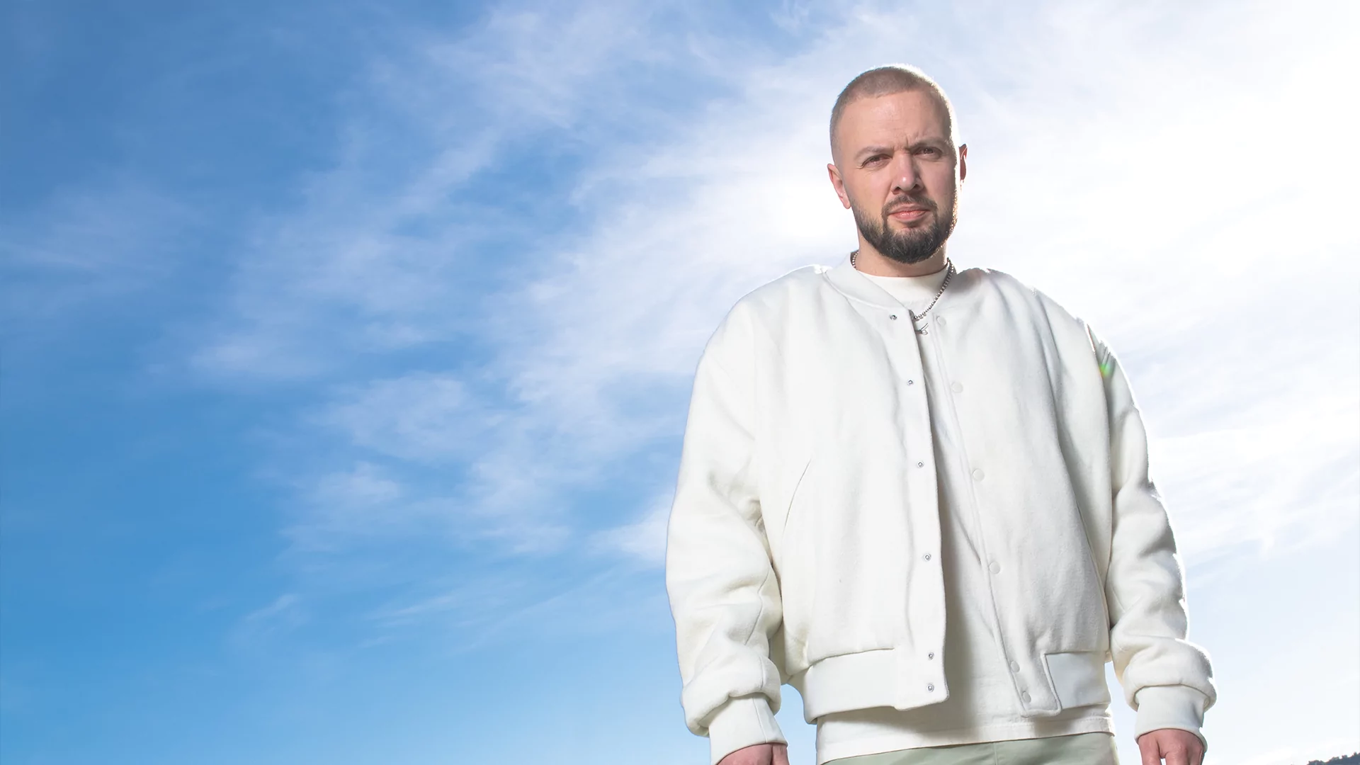 Photo of Chris Lake wearing an all-white outfit posing against the sky.