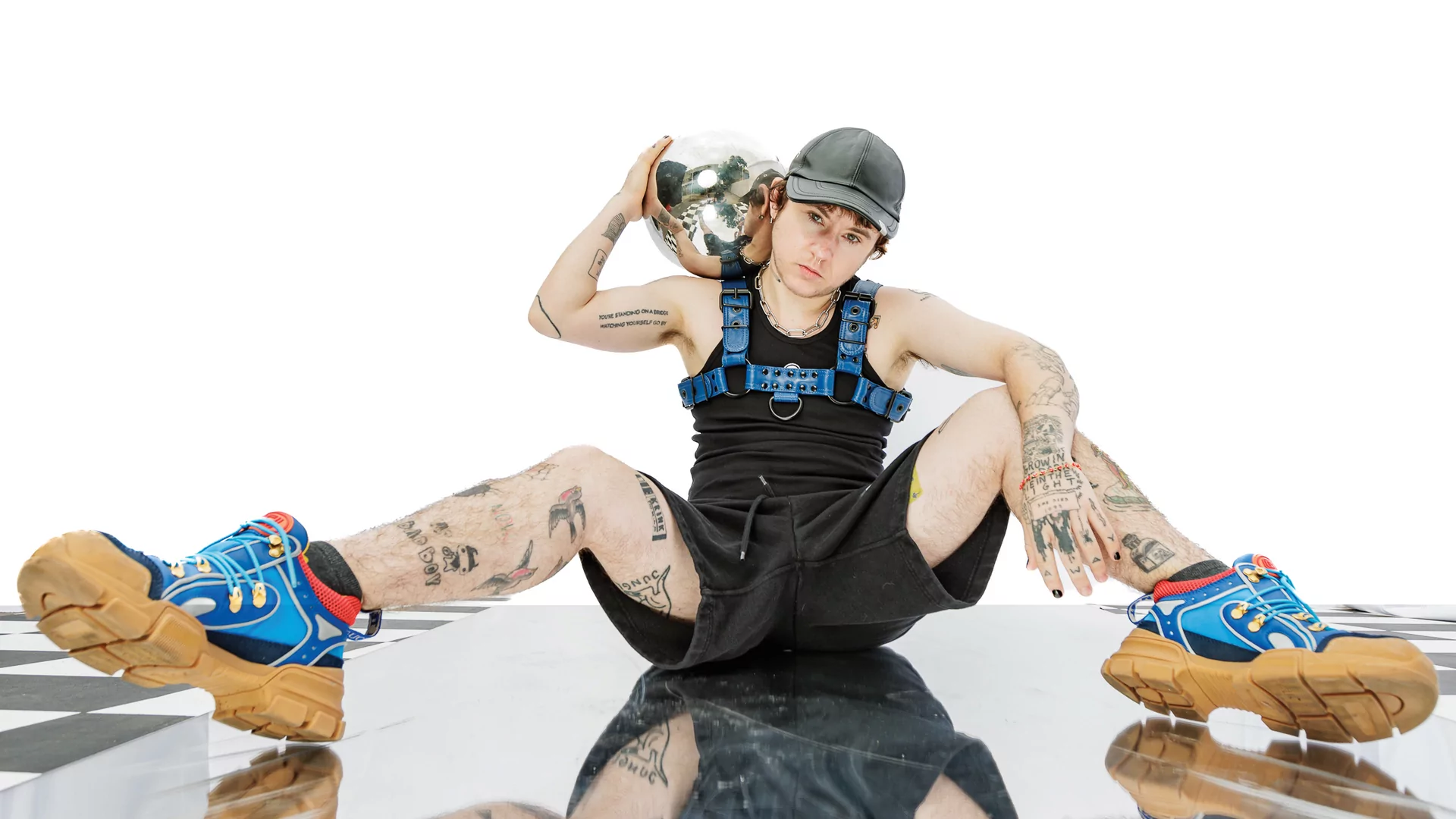 Photo of a.k.a. skips sitting on the floor wearing a blue harness and holding a silver sphere