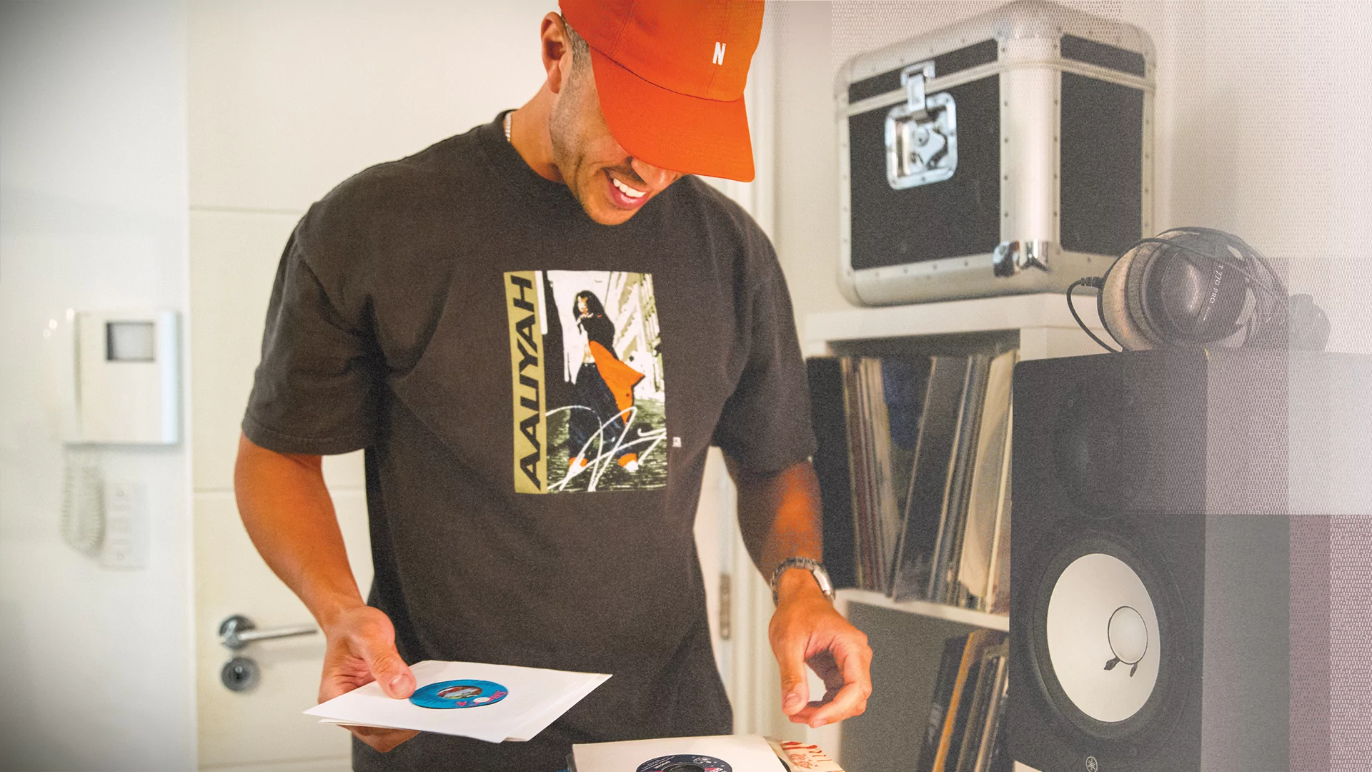 Photo of Melvo Baptiste skimming through records in a studio and wearing a red hat