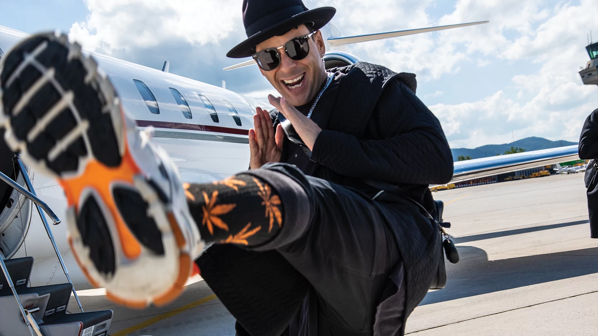 Photo of Timmy Trumpet kicking his foot at the camera in front of a plane