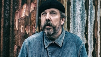 A press photo of Andrew Weatherall in a black hat and blue denim shirt