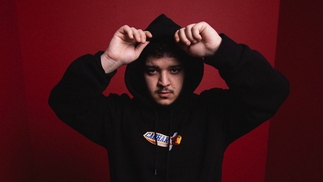 Photo of Bou wearing a black hoodie in front of a red background