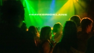 Crowd shot taken inside a club night with the words #SAVEBRICKLANE projected on stage