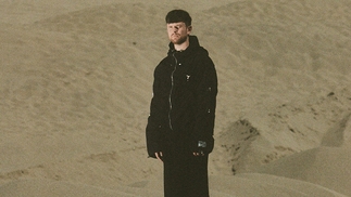 James Blake wears black while posing in a desert