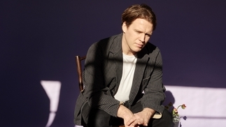 Photo of Tourist sitting on a chair in a purple room wearing a grey pinstriped blazer
