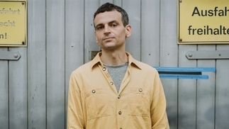 Photo of Barker wearing a yellow shirt and standing in an industrial area