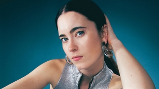Photo of bex wearing a silver top in front of a turquoise background
