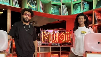 Bradley Zero and Nathanael Williams posing in front of a record collection and neon sign which reads: MOKO