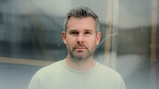 Photo of Voigtmann wearing a cream t-shirt and looking directly at the camera