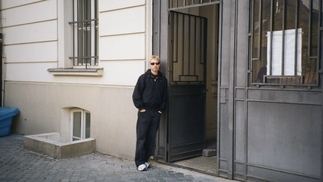 Photo of STEREOMETRIX wearing black jeans, a hoodie and sunglasses while leaning against a door