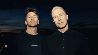 Photo of the two members of Pan-Pot wearing black t-shirts and standing in front of a dark sunset