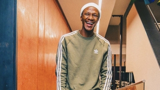 Mdu Aka TRP smiling in a corridor wearing a white beanie hat and green adidas sweater
