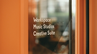 Photo of an orange door with ‘Workspace, Music Studios, Creative Space’ enscripted on the glass
