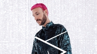 Don Diablo posing in a white room filled with lights. His hair is pink and he's wearing a dark blue sparkling top
