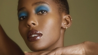 DESIREE wearing blue eyeshadow and framing her face with her hands in front of a green background