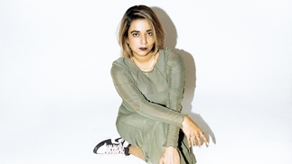 Photo of GoodMostlyBad wearing a green dress and black trainers while sitting on the floor