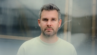 Photo of Voigtmann wearing a cream t-shirt and looking directly at the camera